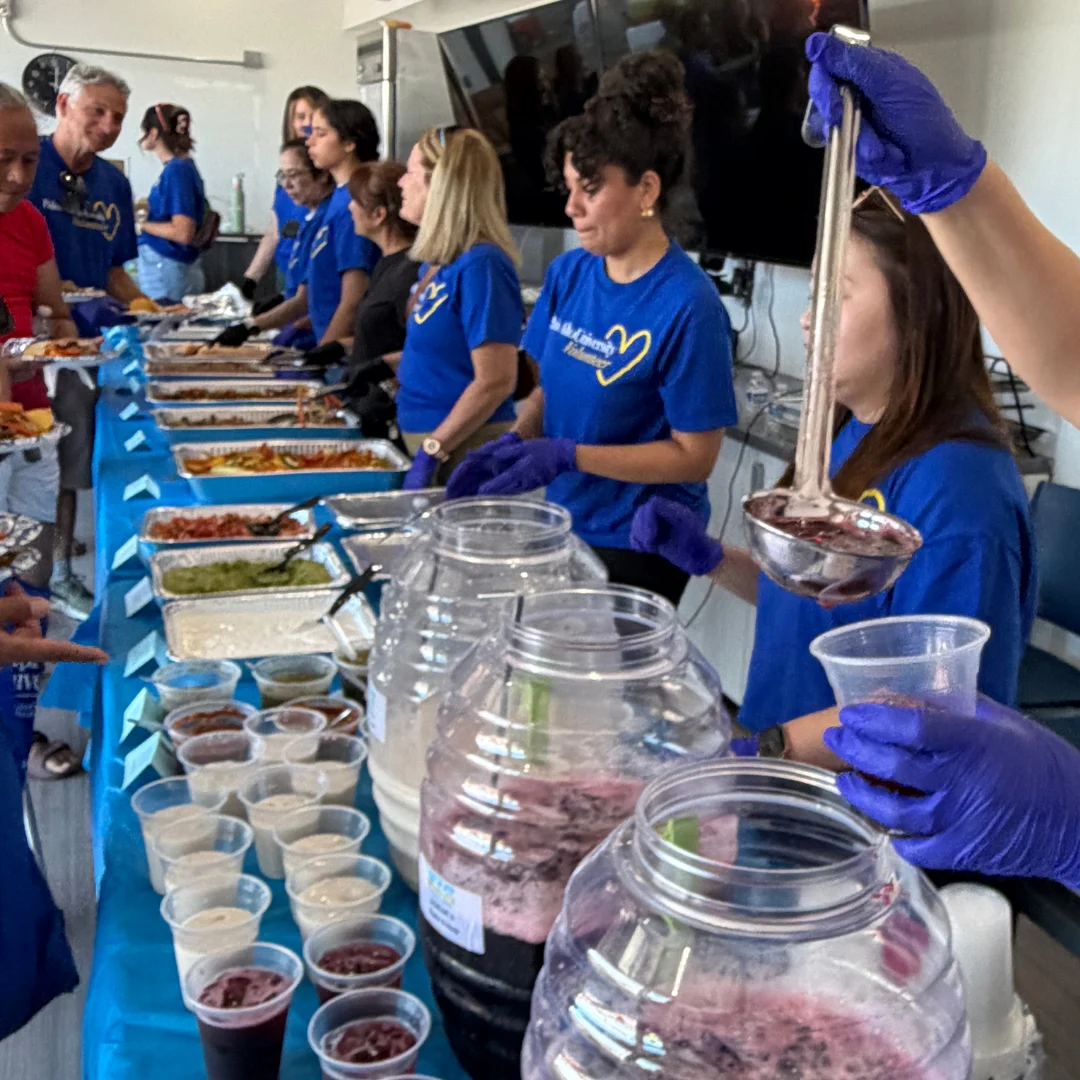 Volunteers in blue Palo Alto University t-shirts and gloves serving food and drinks along a long buffet line at a community service day.